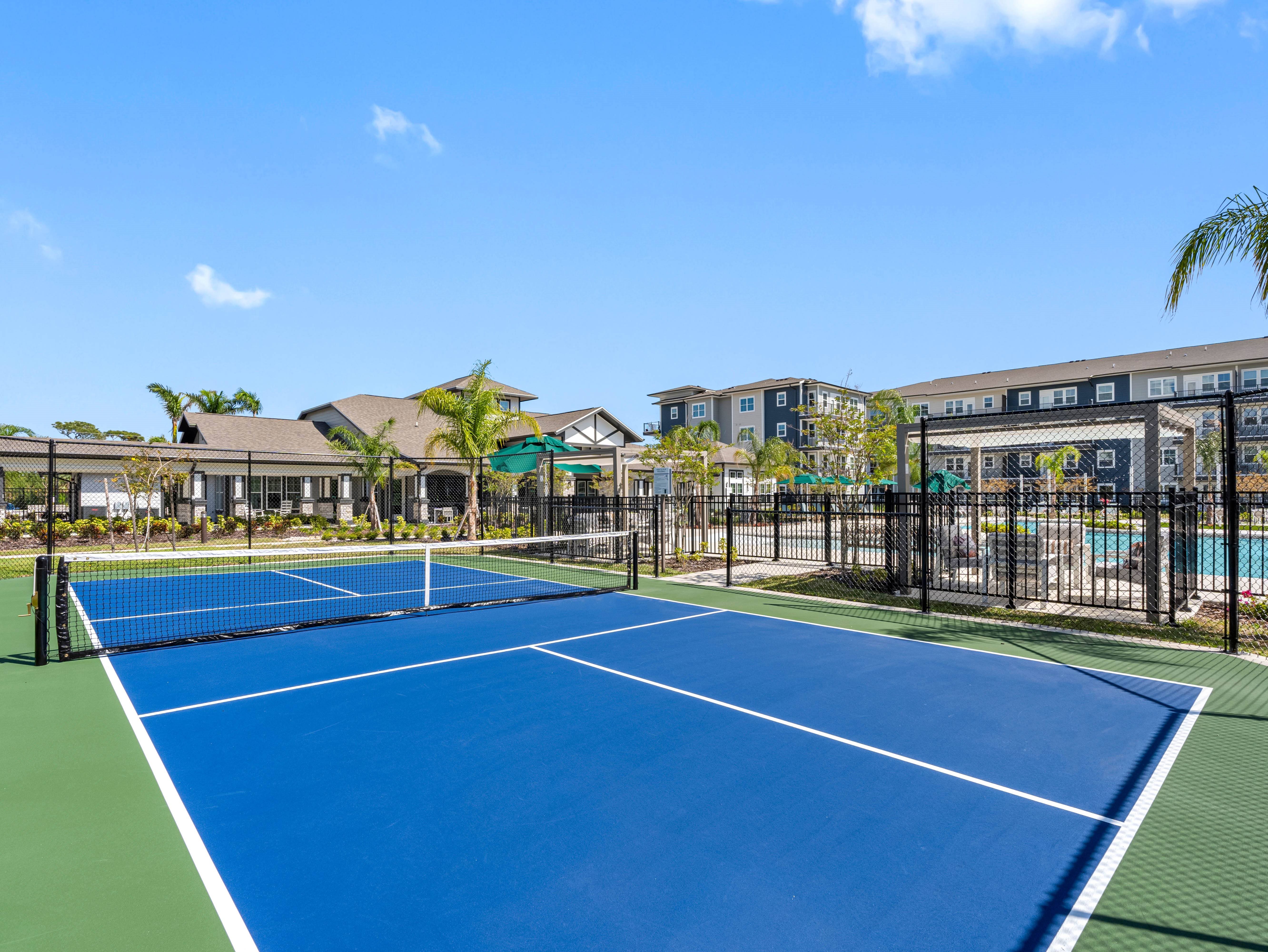 A tennis court with a blue surface and white lines is surrounded by a black fence.